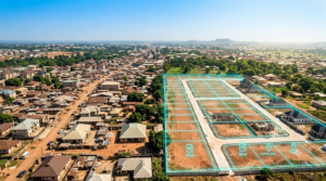Wide aerial landscape shot of a growing Nigerian town (Awka/Onitsha corridor feel) transitioning from older informal buildings on one side to a cluster of neatly gridded, clearly-marked new plots on the other, bright midday sun, vivid blue sky
